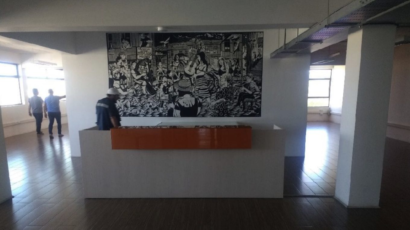 Sala del centro de documentación con un gran mural en blanco y negro, mesón con cubierta naranja y piso de madera