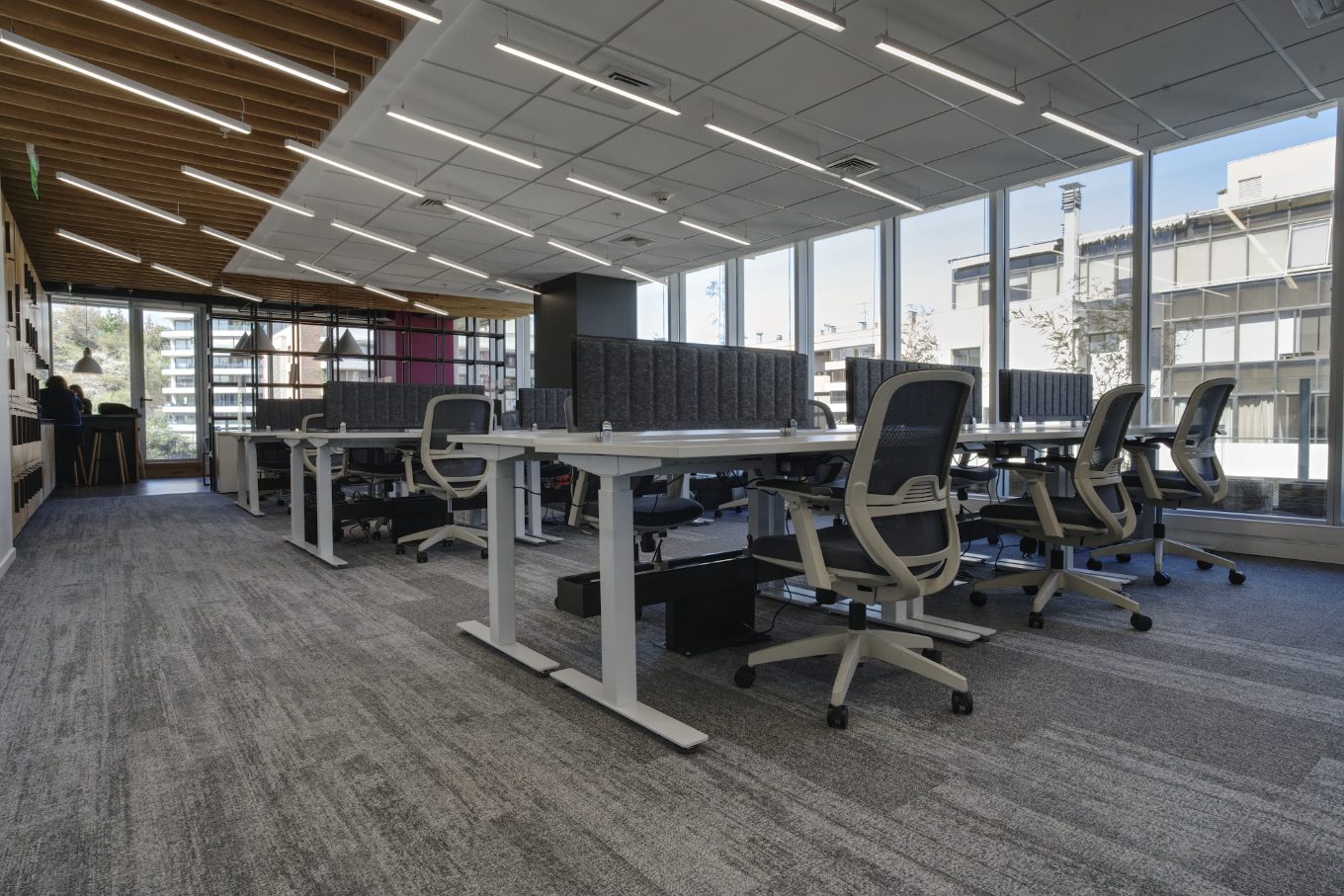 Planta abierta de oficinas con escritorios regulables, sillas ergonómicas, paneles acústicos y ventanales
